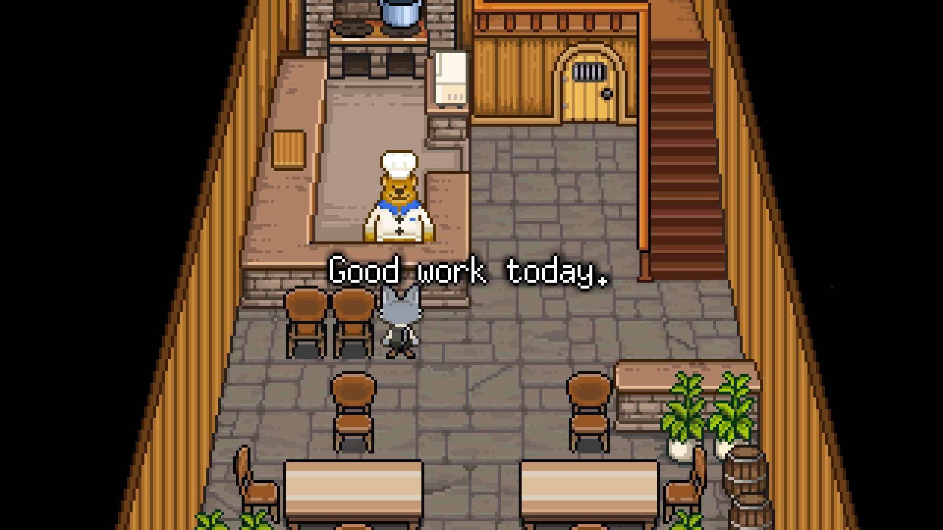 A screenshot from the game, set again inside of Bear's restaurant. Bear stands behind the counter, while Cat standsin front of the counter facing him. more of the kitchen area can be seen, revealing a stove against the back wall, and a microwave to its right on the counter. A cutting board sits on the left counter. There are no customers, and there is white pixelated text with a black outline. It reads: Good work today.