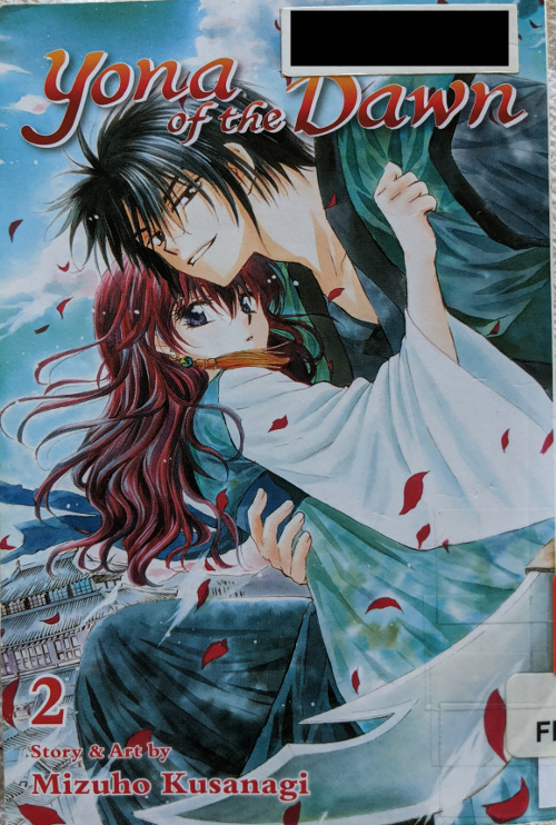 Cover for Yona of the Dawn Volume 2. Yona is being carried by Hak, with red petals swirling around them. They appear to be in the sky, as the palace can be seen below them in the background.