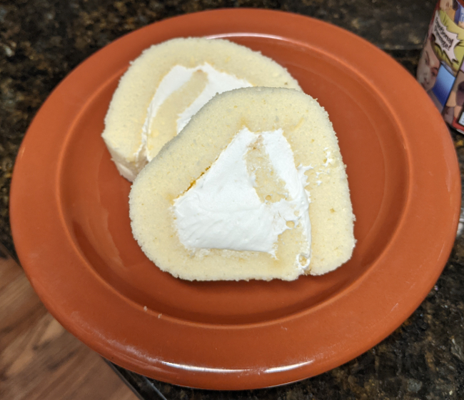 A round brown plate with two slices of roll cake, one slightly on top of the other.