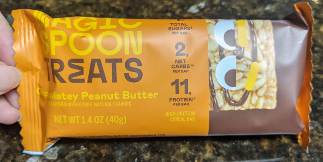A single bar treat bar, still in package. Has the same text as the outer box. On the right side of the package there is the same cereal bar with eyes.
